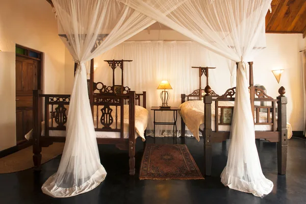 Carved Zanzibar-style beds under white canopies